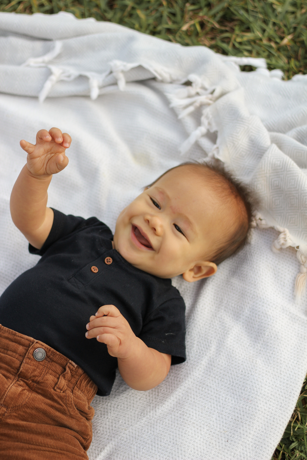 Baby laughing while lying on a white blanket in the grass, Kauaʻi