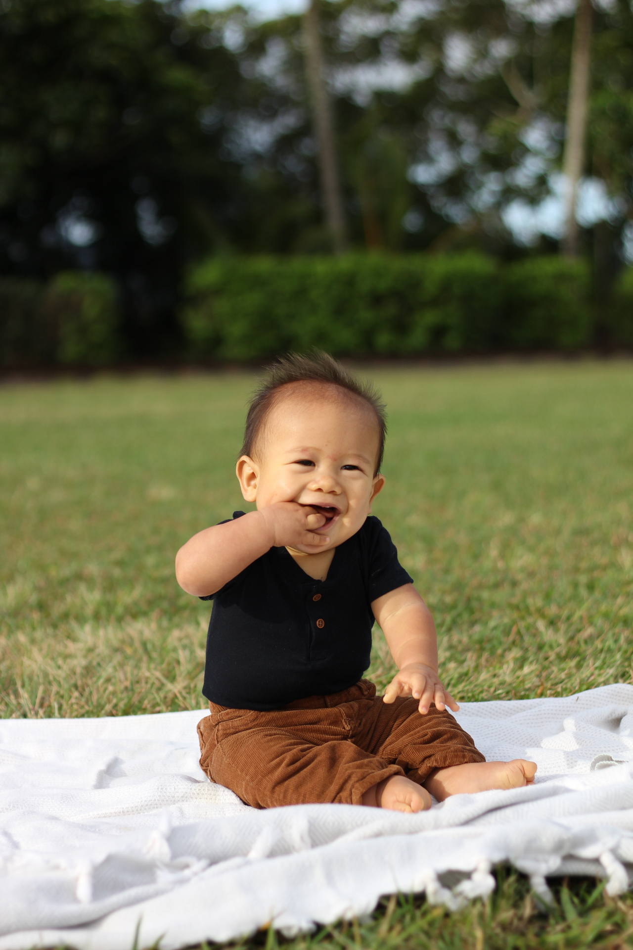 Baby sitting on a blanket in the grass, smiling at golden hour, Kauaʻi