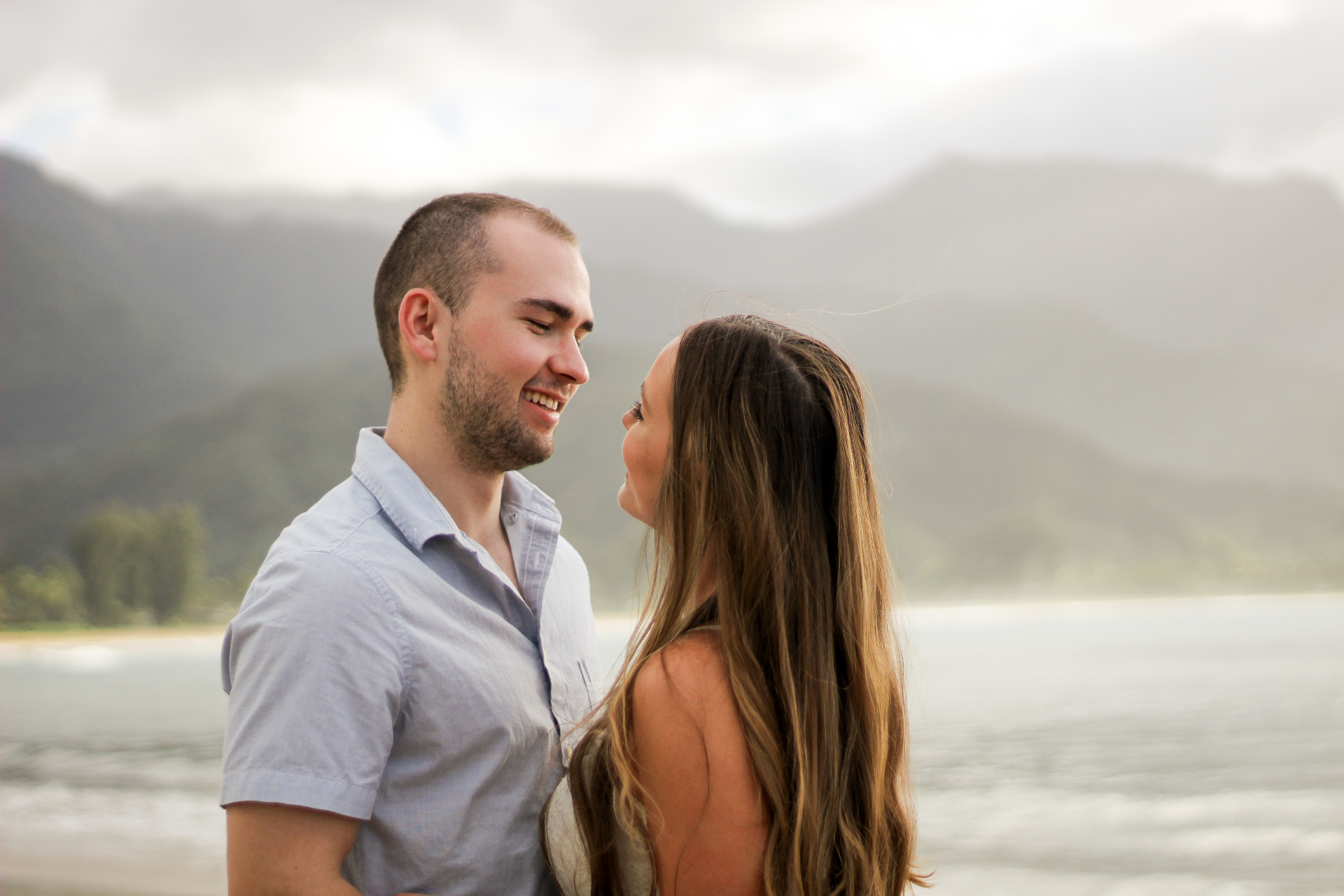 Couple smiling at each other with Hanalei Bay and mountains in the background, Kauaʻi