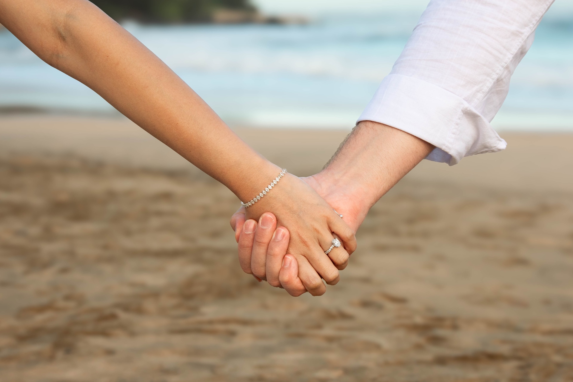 Close-up of couple holding hands on the beach with engagement ring, Kauaʻi