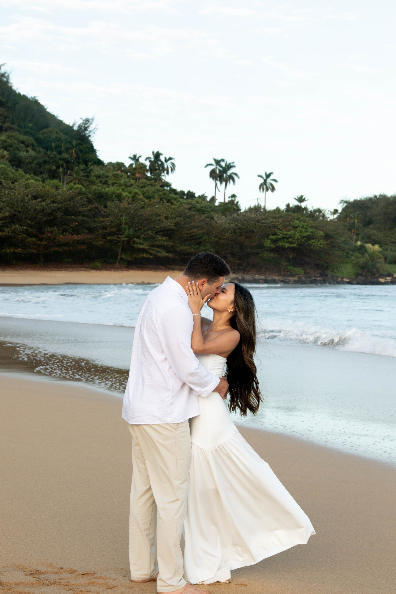 Couple kissing at the shoreline in white attire, Kauaʻi