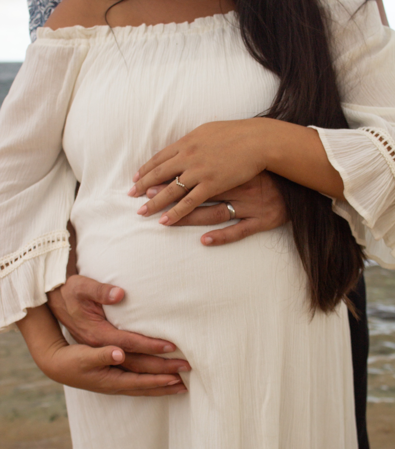 Close-up of hands resting on a baby bump at the beach