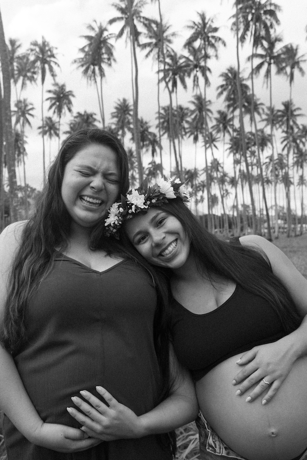 Black and white maternity portrait of two sisters under palm trees