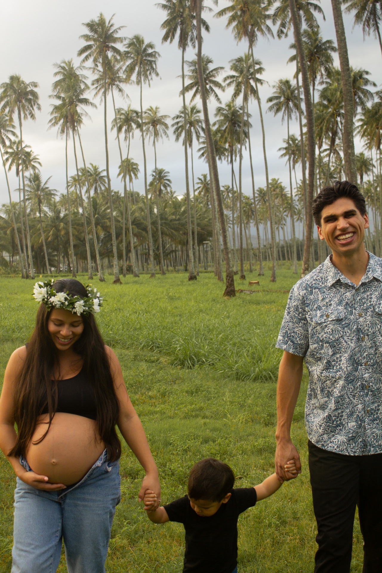 Expecting parents walking with toddler through a palm grove