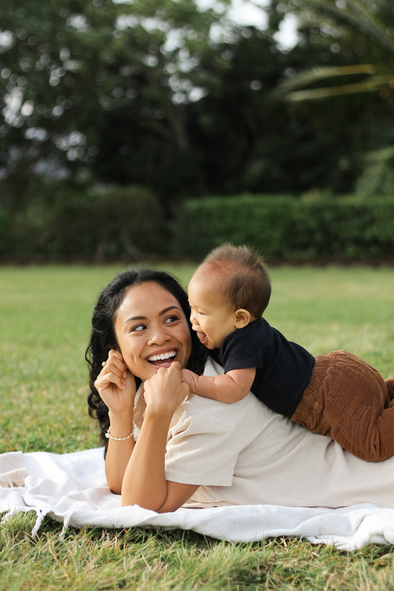 Mother laughing with baby on a blanket in the grass