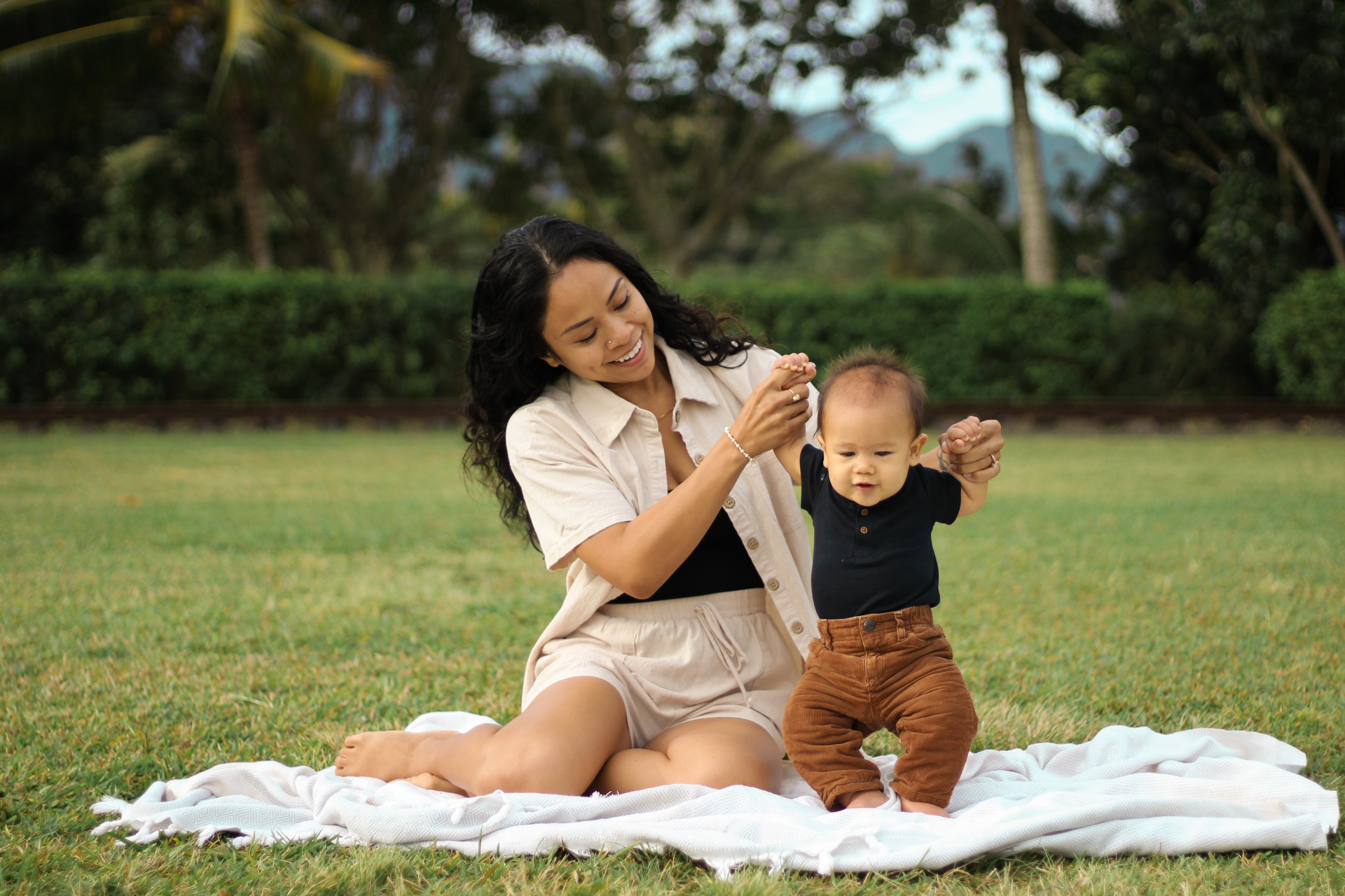 Mother helping her baby stand on a blanket in the grass