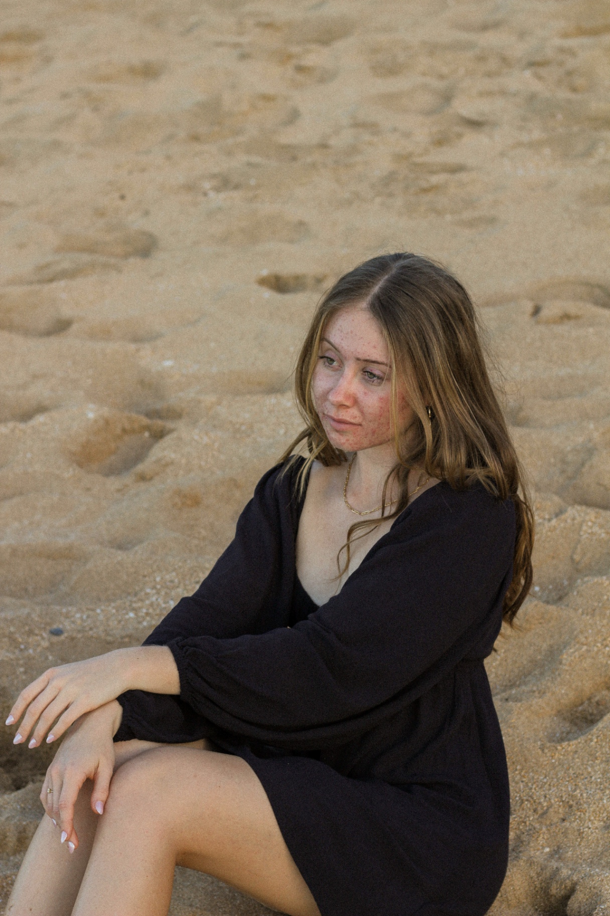 Portrait in black dress seated on soft sand at golden hour, Kauaʻi