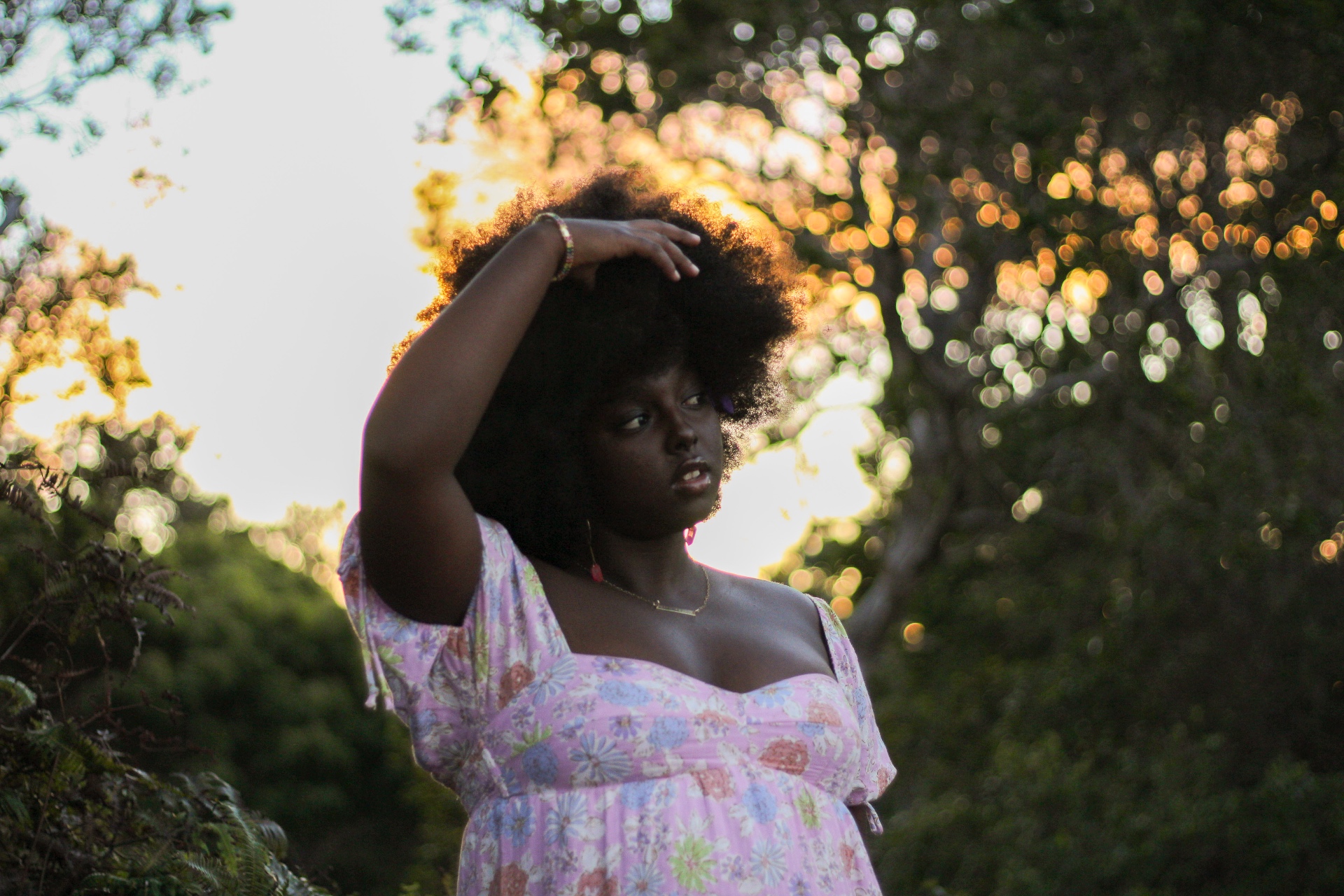 Portrait in floral dress with golden bokeh light through trees at sunset, Kauaʻi