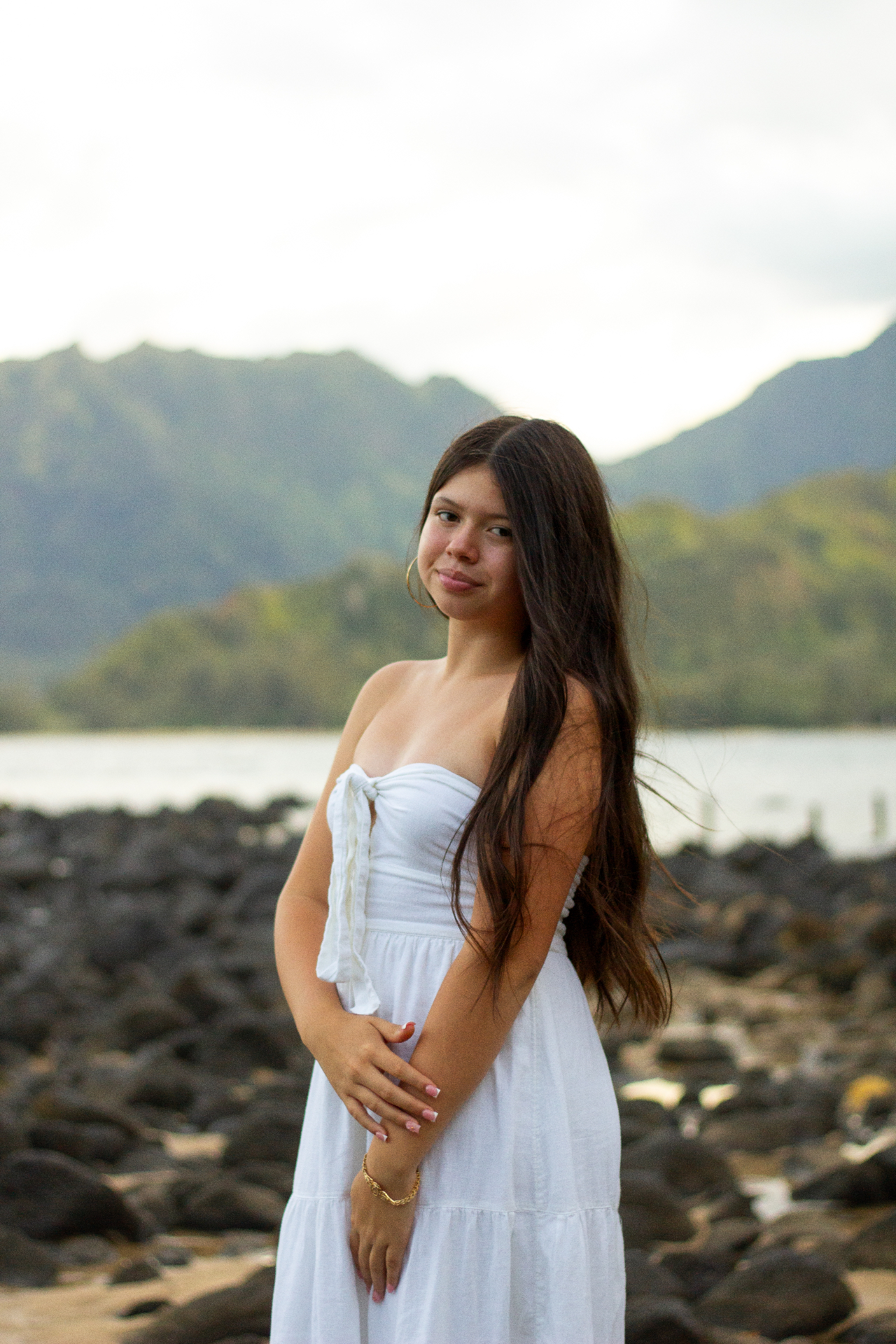 Portrait in white dress on lava rocks with Hanalei mountains behind, Kauaʻi