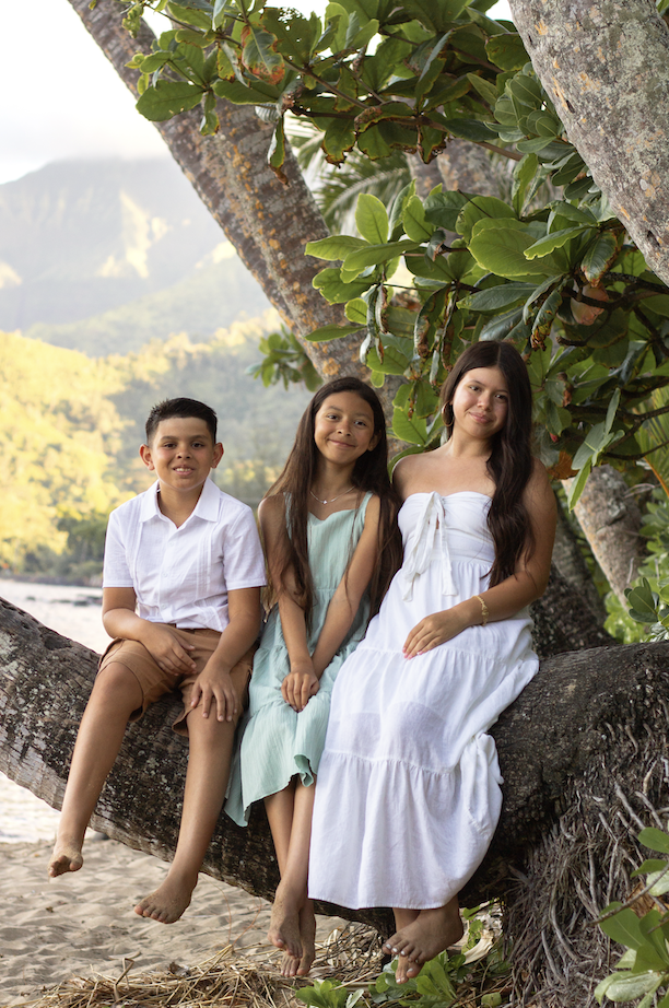 Three siblings sitting on a palm tree by the shore