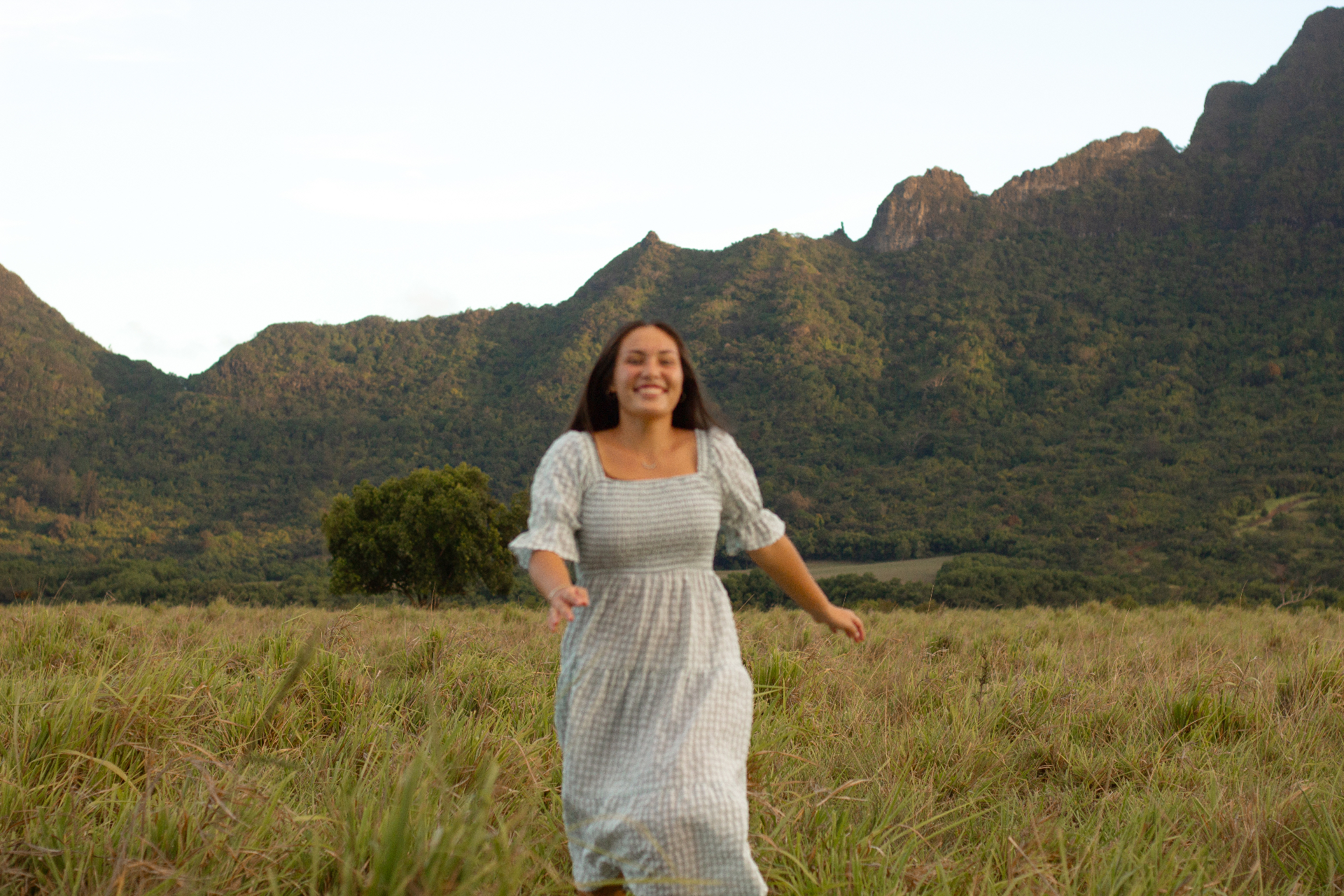 Joyful portrait running through a meadow with mountains behind, Kauaʻi