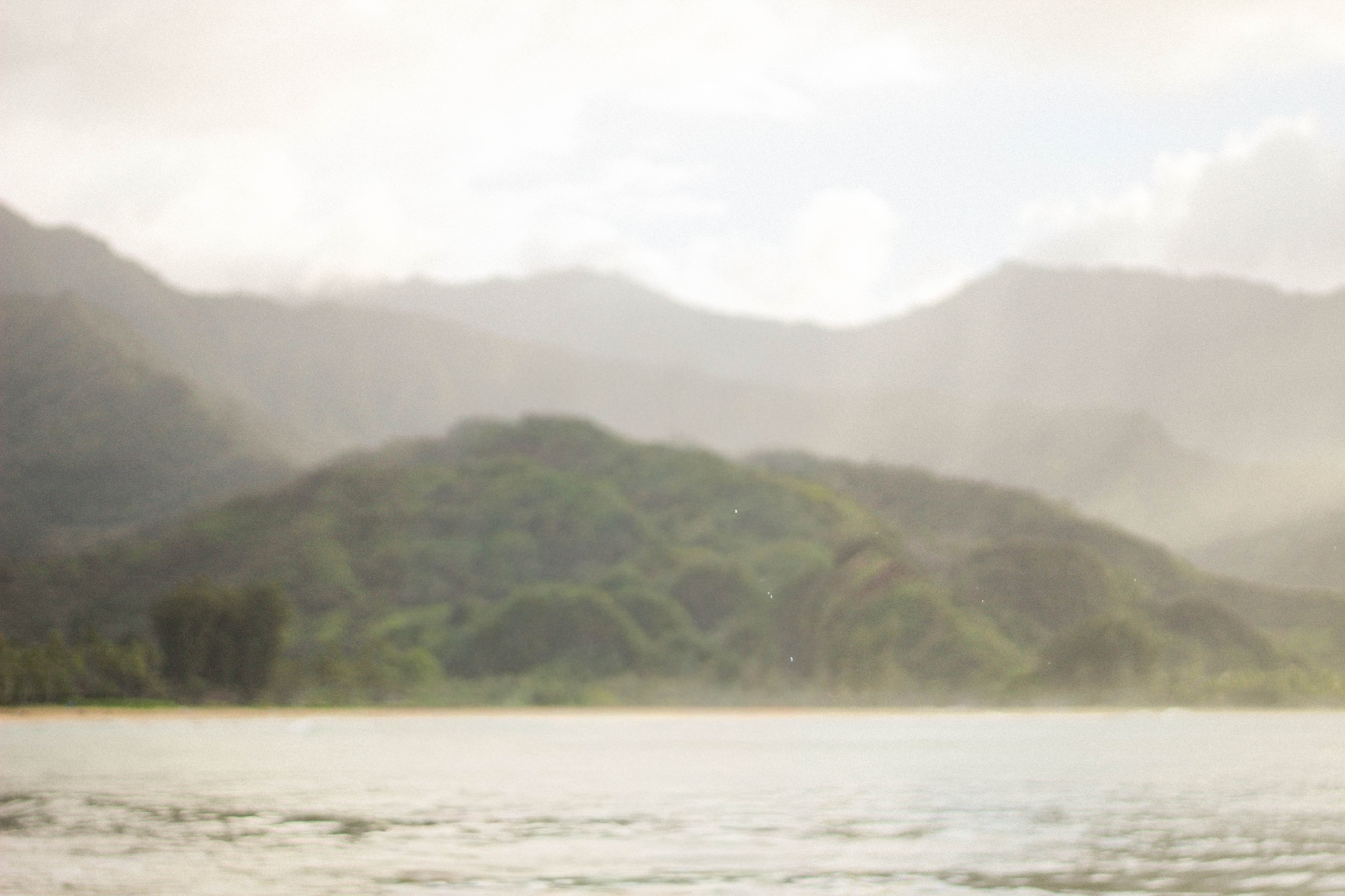 Leilani crouched on lava rocks at the water's edge with Kauaʻi mountains at sunrise